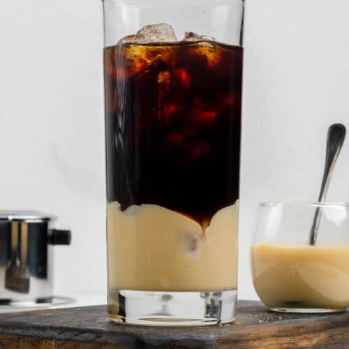 Vietnamese iced coffee in a tall glass and a small bowl of sweetened condensed milk.