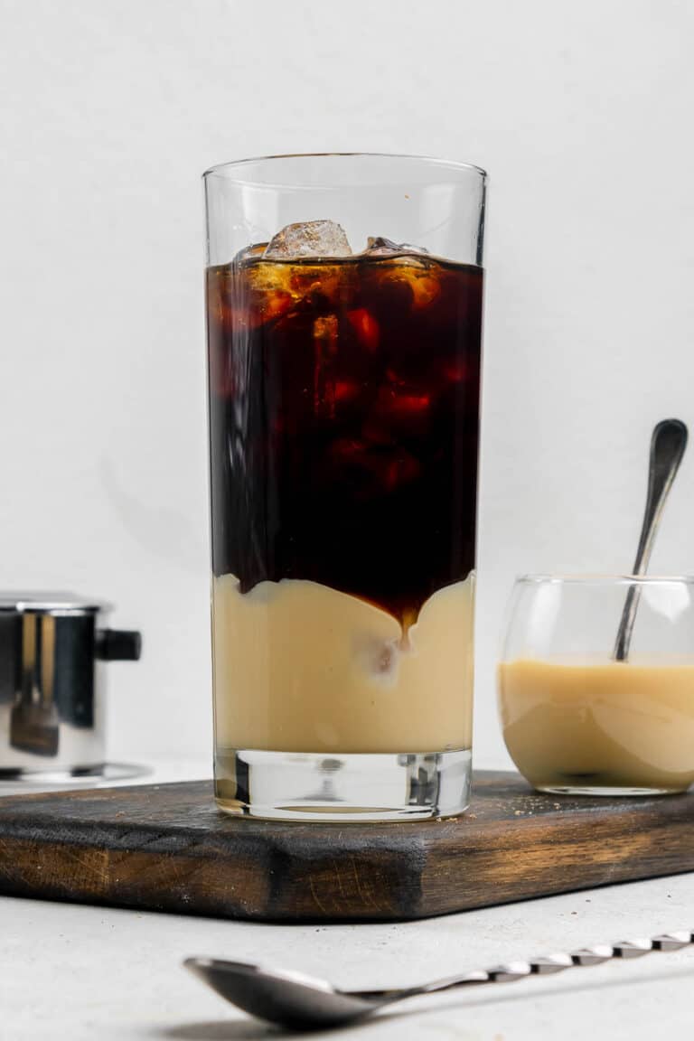Vietnamese iced coffee in a tall glass and a small bowl of sweetened condensed milk.