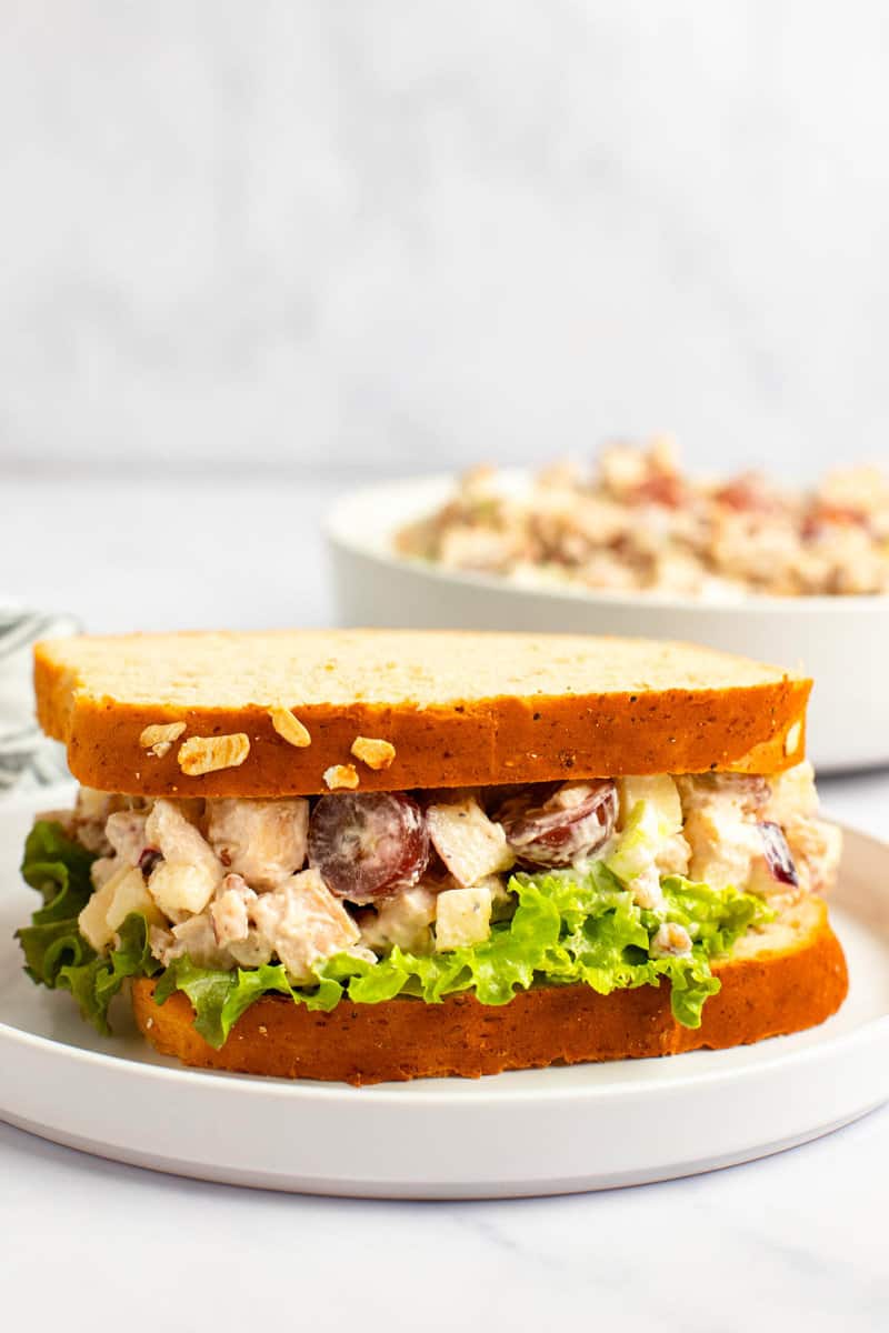 Copycat Arby's pecan chicken salad sandwich on a plate and the salad in a bowl behind it.