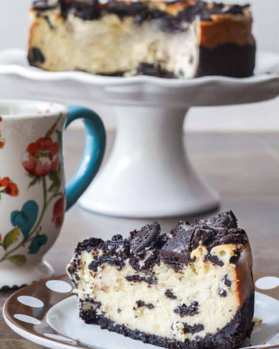 Copycat Cheesecake Factory Oreo Cheesecake slice and the dessert behind it on a cake stand.