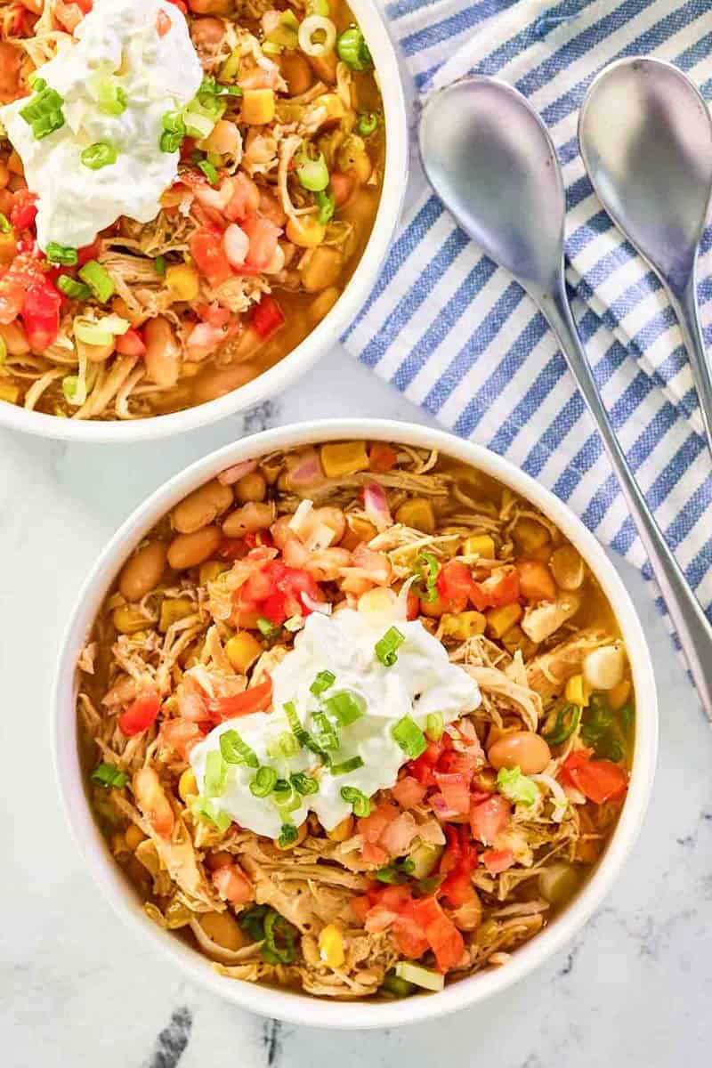 Crockpot white chicken chili garnished with sour cream and green onions in two bowls.