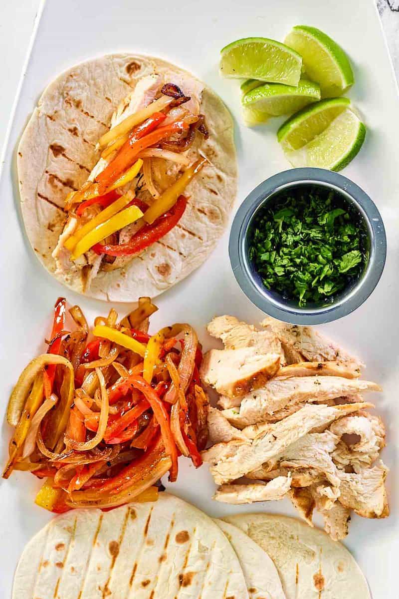 Grilled chicken fajitas, lime wedges, and chopped cilantro on a platter.