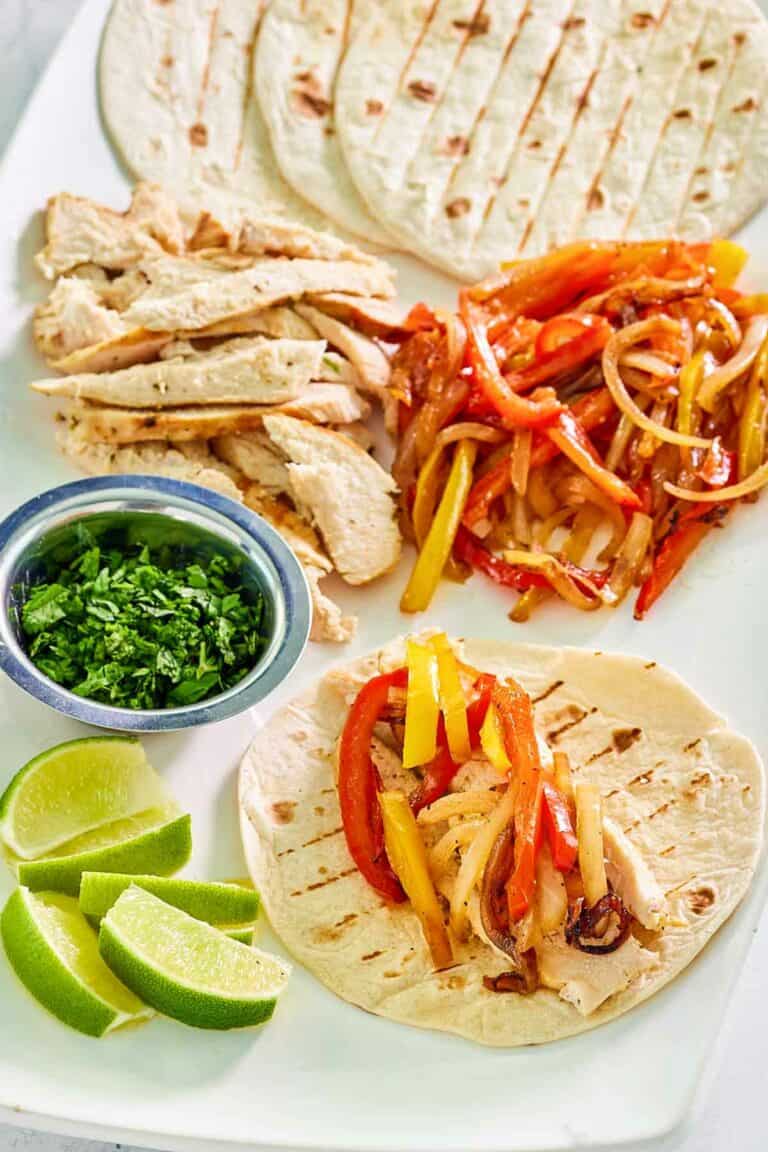 Grilled chicken fajitas, a cup of chopped cilantro, and lime wedges.