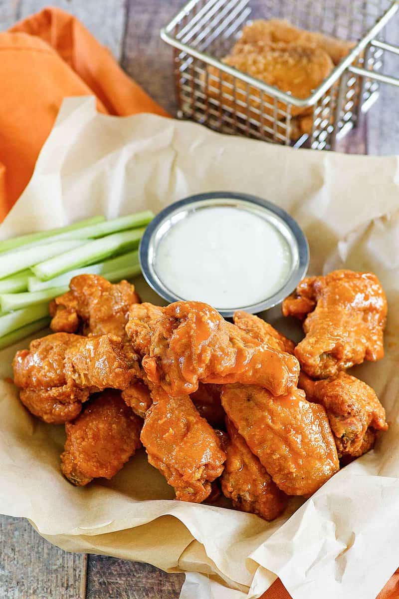 Copycat Hooters wings, celery sticks, and a cup of dipping sauce in a serving basket.