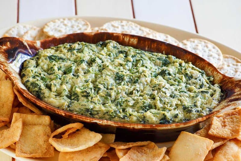 Copycat Houston's spinach artichoke dip, pita chips, and crackers on a platter.