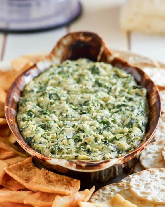 Copycat Houston's spinach artichoke dip on a platter with pita chips and crackers.