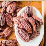 Spiced pecans on a large spoon and baking sheet.