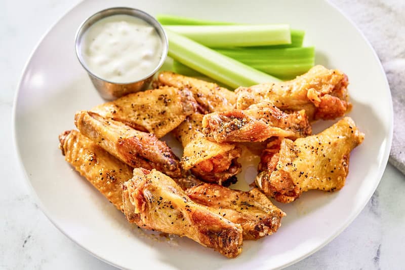 Copycat Wingstop lemon pepper wings, celery sticks, and dipping sauce on a plate.