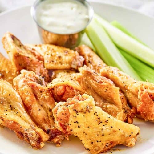 Copycat Wingstop lemon pepper wings, celery, and dipping sauce on a plate.