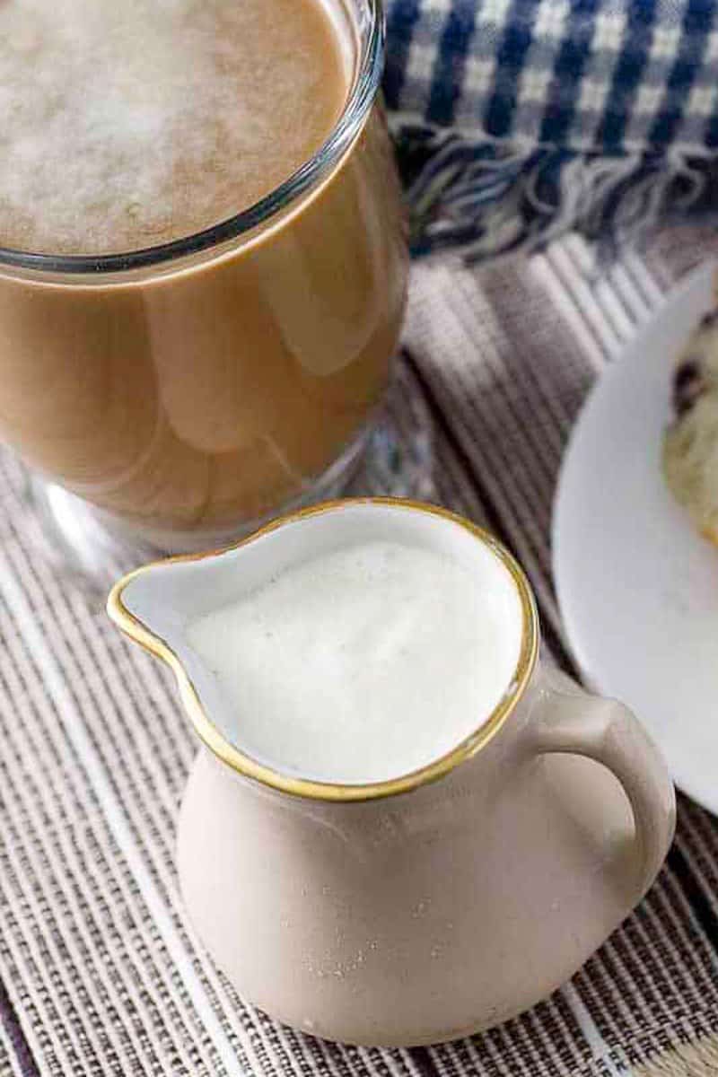 Homemade French vanilla coffee creamer in a small pitcher next to a cup of coffee.