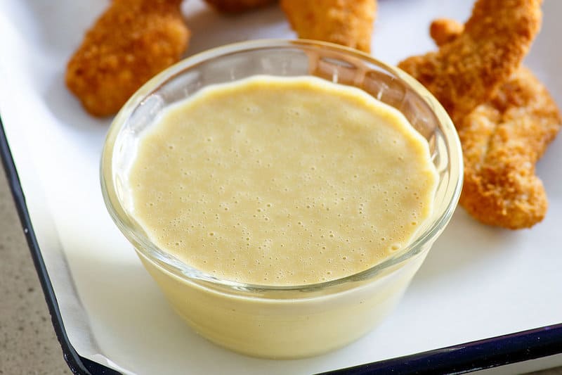 A bowl of copycat Outback Steakhouse honey mustard and chicken fingers on a tray.