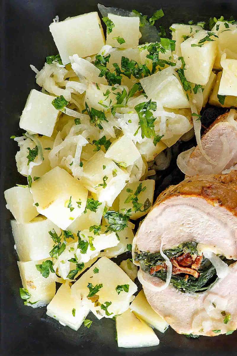 Buttery parsley potatoes with onions and stuffed pork loin on a plate.