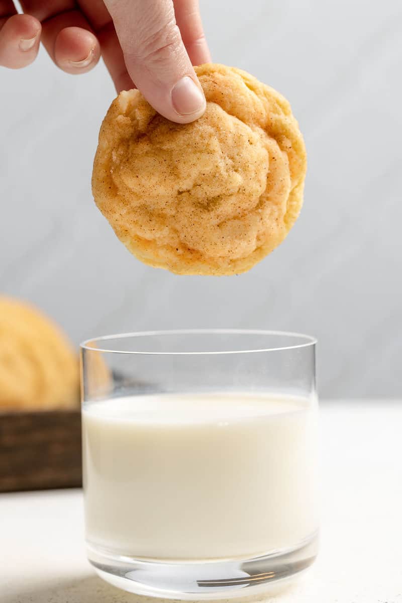 A snickerdoodle cookie being held over a glass of milk.
