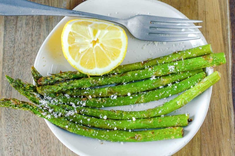 Air fryer asparagus, lemon wedge, and fork on a plate.