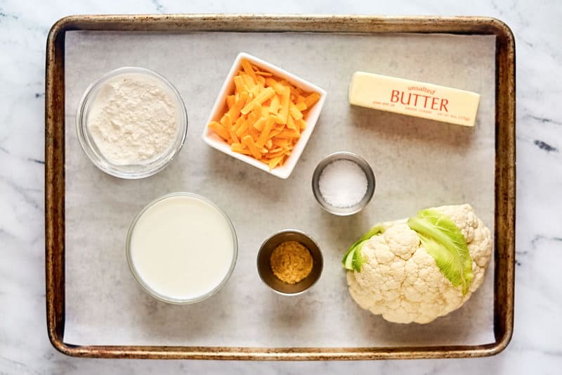Baked cauliflower with cheese sauce ingredients on a tray.