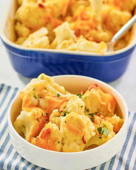 Baked cauliflower with cheese sauce serving in a bowl in front of the dish.