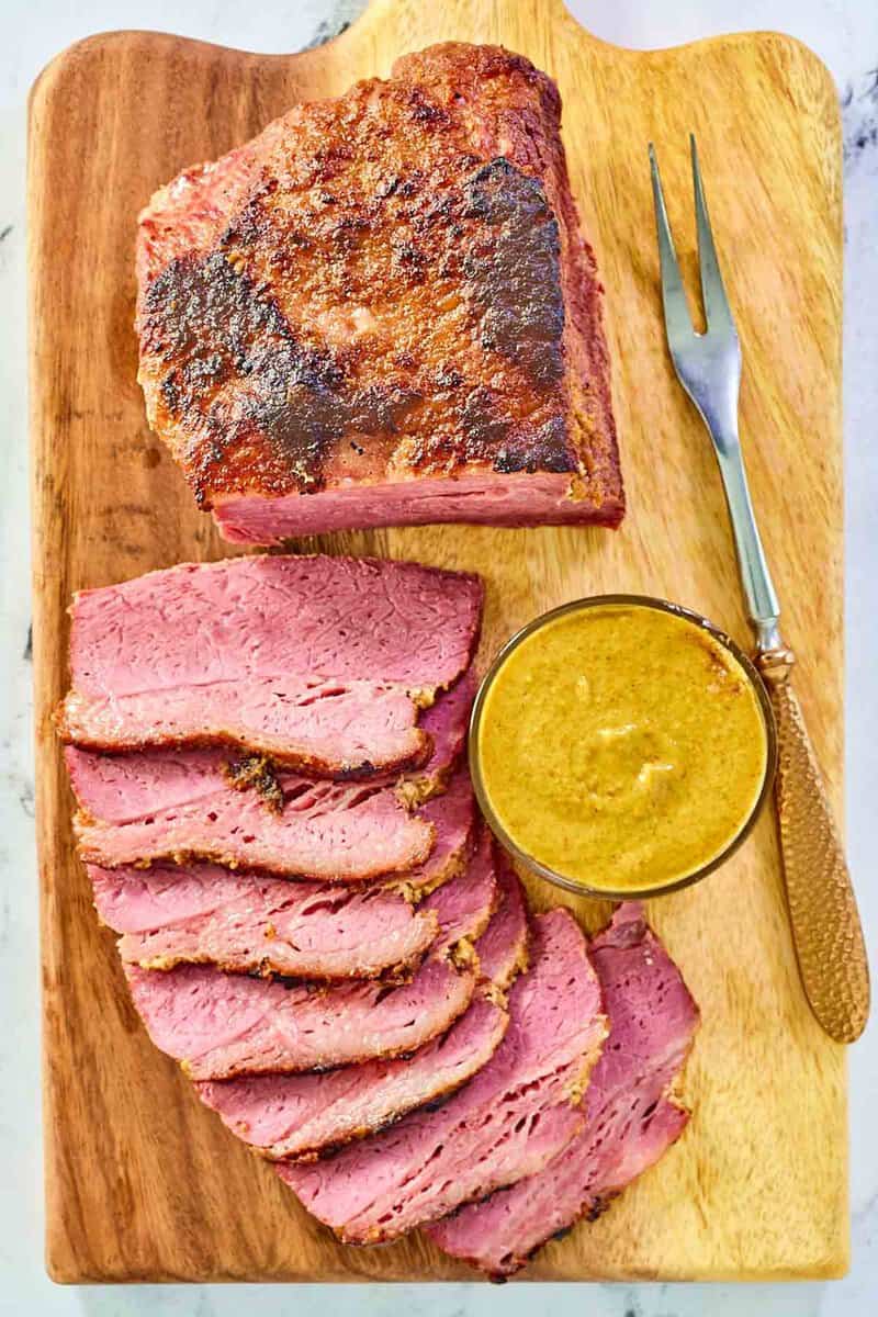 Baked corned beef slices, small bowl of mustard, and a carving fork.