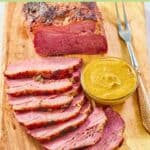 Baked corned beef, a small bowl of mustard, and a carving fork.