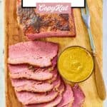 Baked corned beef slices, bowl of mustard, and a carving fork.