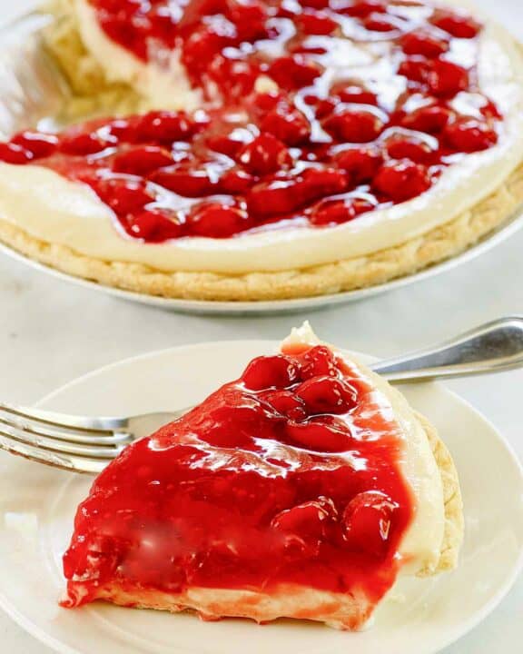 Slice of cherry cream cheese pie on a plate and the pie behind it.