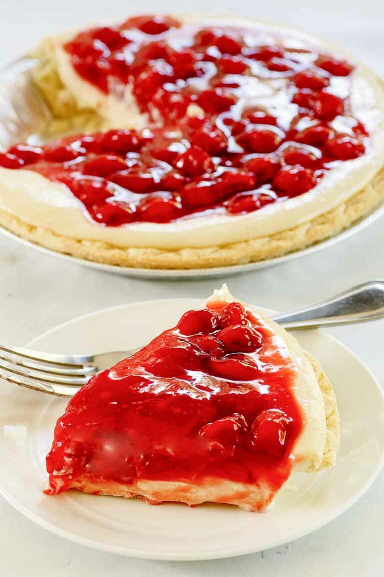 Slice of cherry cream cheese pie on a plate and the pie behind it.