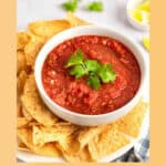 A bowl of homemade Chili's salsa garnished with fresh cilantro and tortilla chips.
