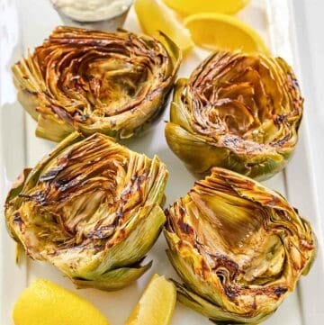 Grilled artichokes, garlic aioli, and lemon wedges on a platter.