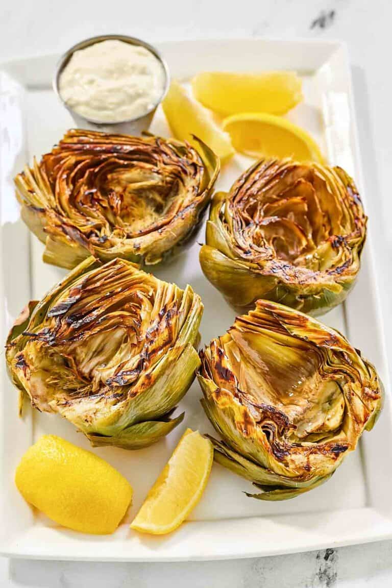 Grilled artichokes, garlic aioli, and lemon wedges on a platter.