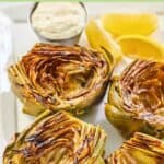 Several grilled artichoke halves and a cup of garlic aioli.