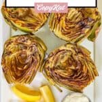 Grilled artichokes, lemon wedges, and a cup of garlic aioli on a platter.