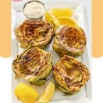Grilled artichoke halves, garlic aioli, and lemon wedges on a platter.