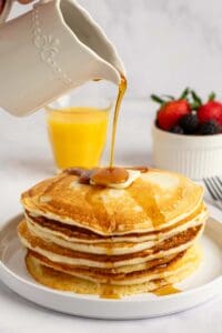 Pouring syrup over copycat IHOP buttermilk pancakes on a plate.