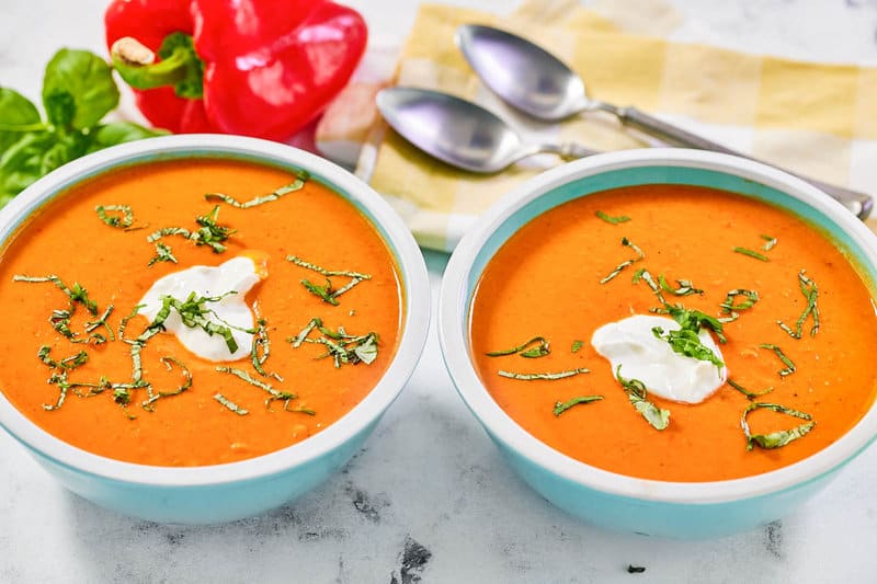 Copycat La Madeleine red pepper soup in two bowls and two spoons behind them.