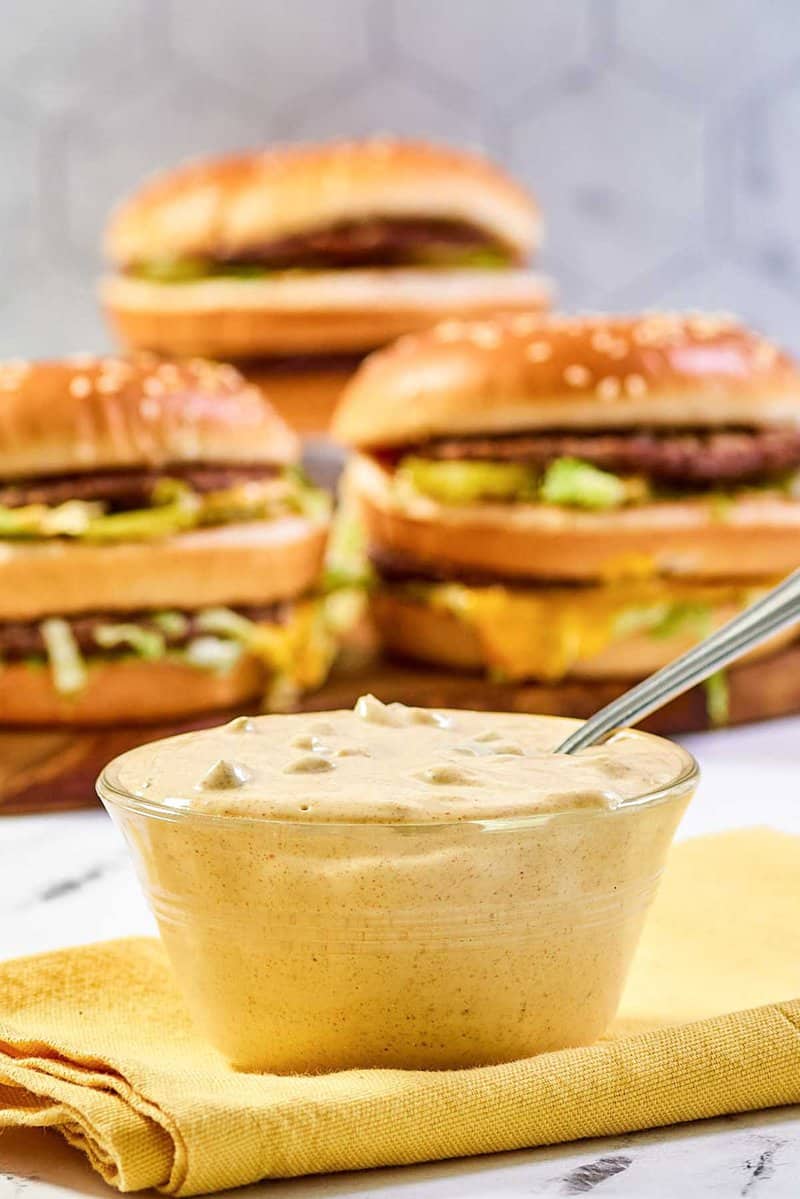 A bowl of copycat McDonald's big mac sauce and three burgers behind it.