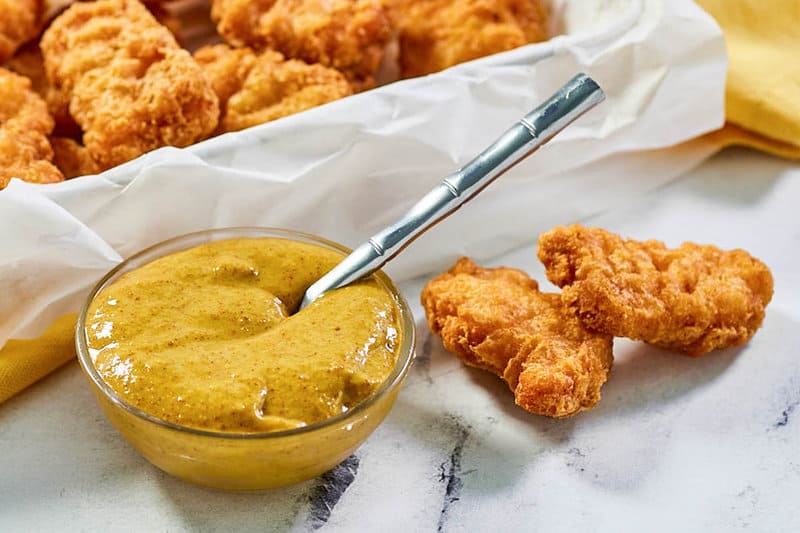 A bowl of copycat McDonald's hot mustard sauce and chicken nuggets next to it.