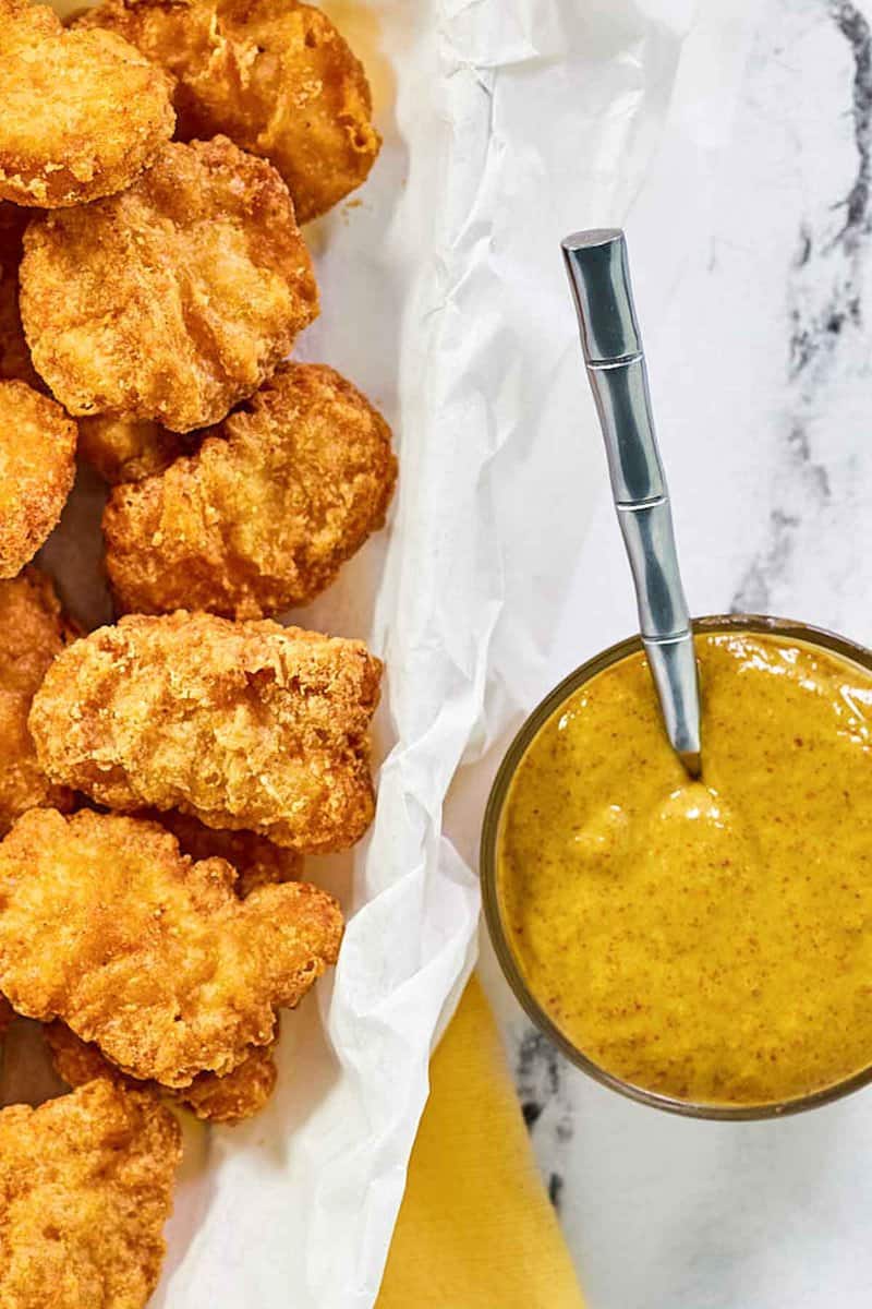 Copycat McDonald's hot mustard sauce in a bowl next to a basket of chicken nuggets.