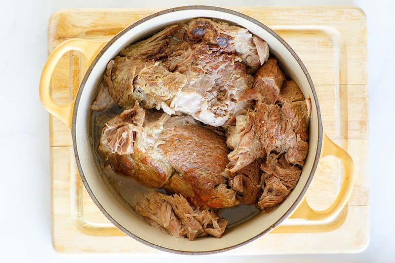 Cooked pork carnitas meat in a Dutch oven.