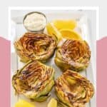 Four grilled artichokes and a cup of homemade garlic aioli on a platter.