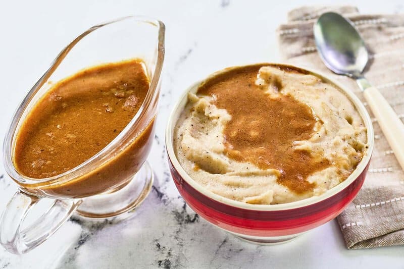 Copycat KFC gravy in a gravy boat next to a bowl of mashed potatoes with gravy.