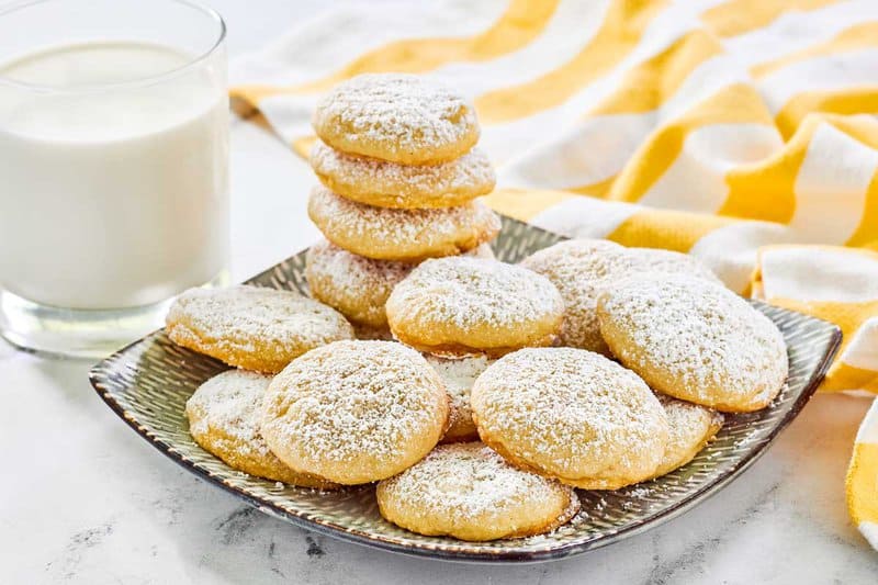 Copycat Panera lemon drop cookies on a plate and a glass of milk next to it.