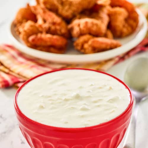 A bowl of copycat Red Lobster pina colada coconut shrimp sauce and coconut shrimp behind it.