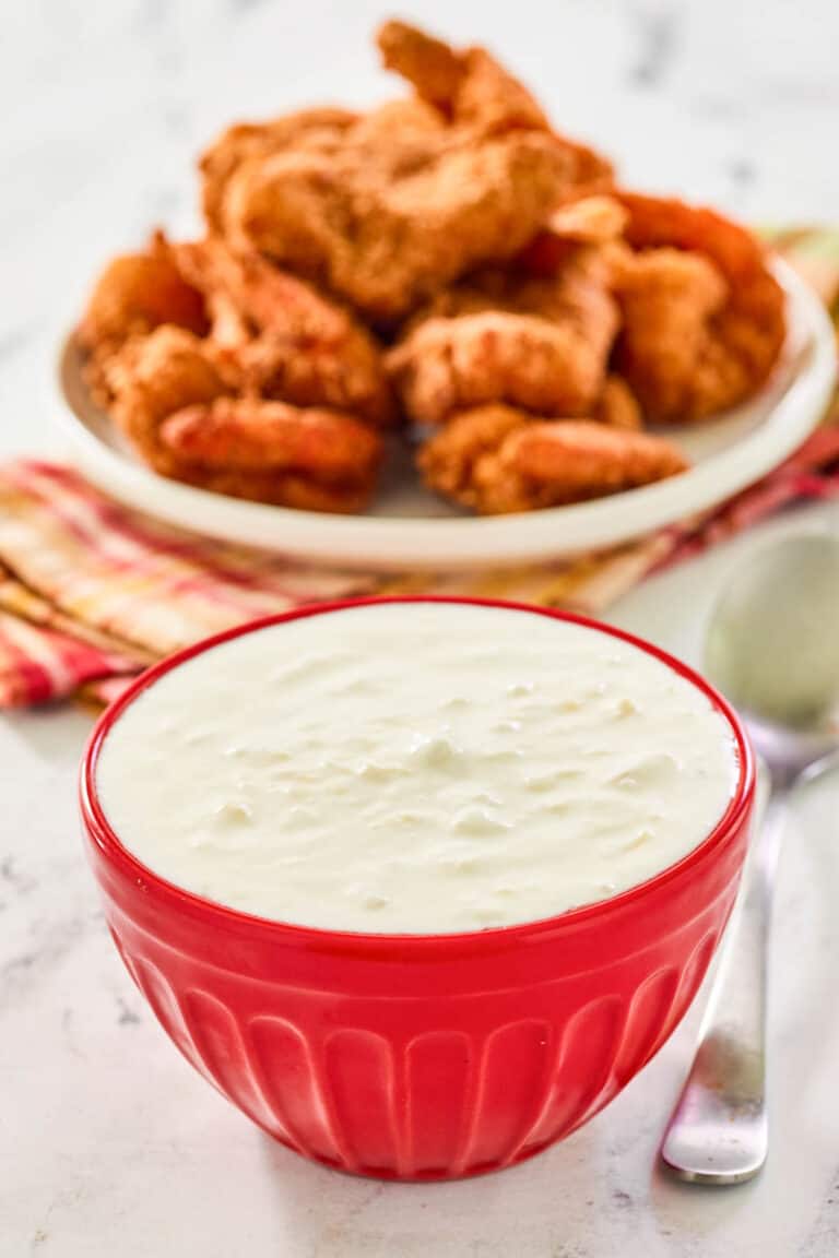A bowl of copycat Red Lobster pina colada coconut shrimp sauce and coconut shrimp behind it.