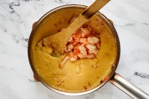 Adding lobster and shrimp to cheese fondue mixture in a pan.