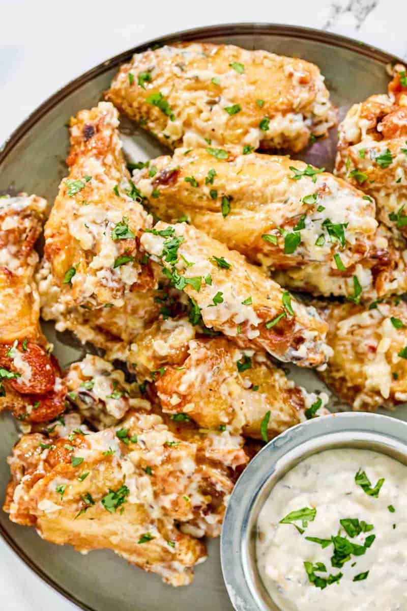 Copycat Buffalo Wild Wings garlic parmesan wings and a cup of the sauce on a plate.