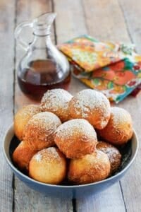 Copycat Denny's pancake puppies in a bowl and a bottle of syrup.