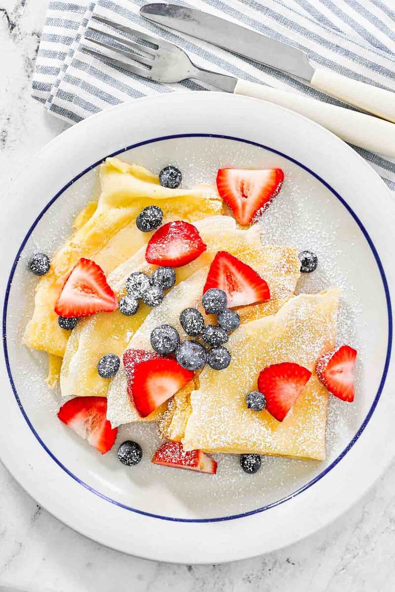 Copycat IHOP fresh berry crepes on a plate and a knife and fork beside it.