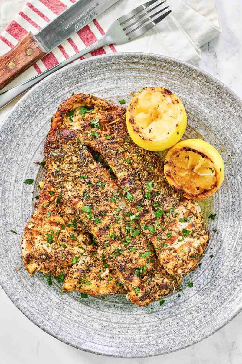 Copycat Texas Roadhouse herb crusted chicken and grilled lemon halves on a plate.