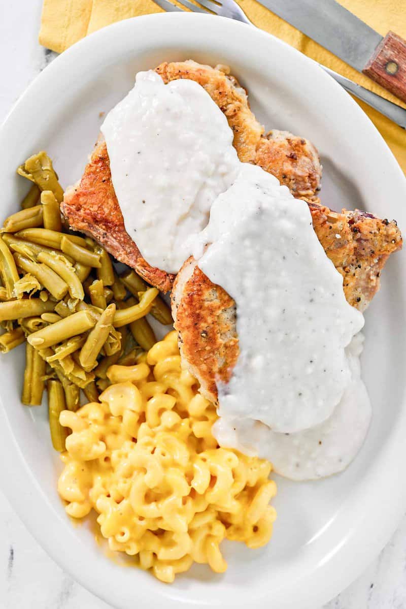 Two copycat Cracker Barrel country fried pork chops with gravy.