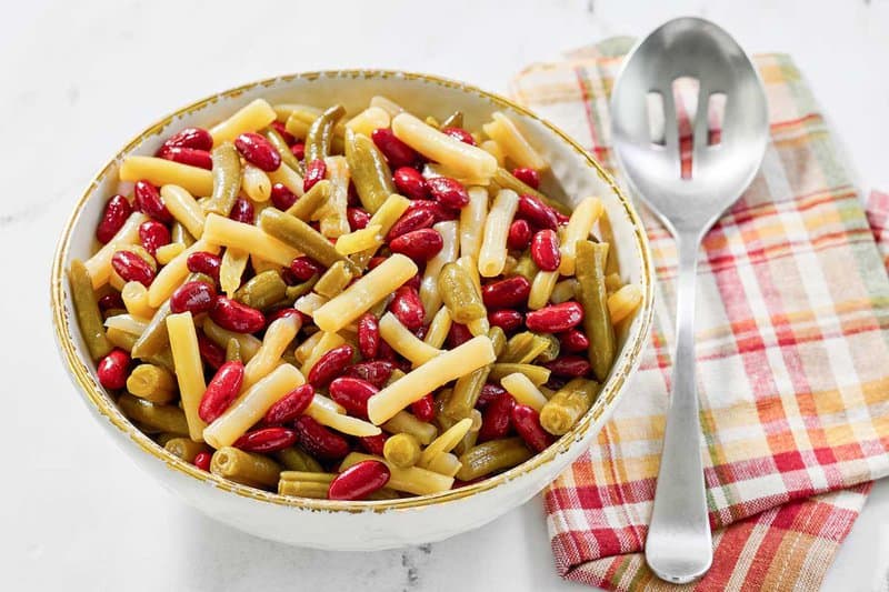 A bowl of grandma's three bean salad and a slotted spoon next to it.