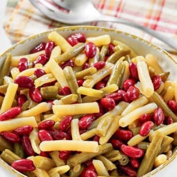 Grandma's three bean salad in a serving bowl and a slotted spoon on a napkin.